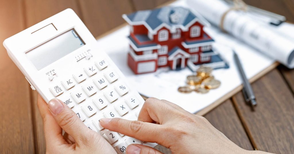 Woman using a calculator in front of a house model to calculate home equity