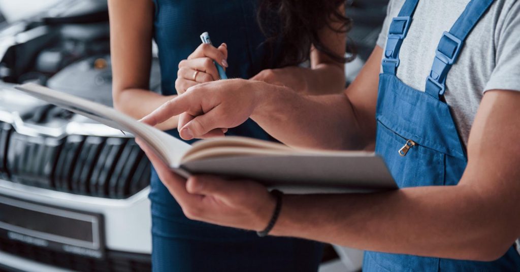 Woman reviewing paperwork with a mechanic beside a car