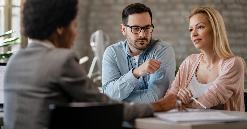 Two people discussing documents with another person across a desk