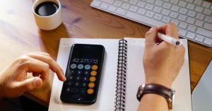 Entrepreneur working from home with calculator and papers, calculating early loan payoff strategies to save interest.