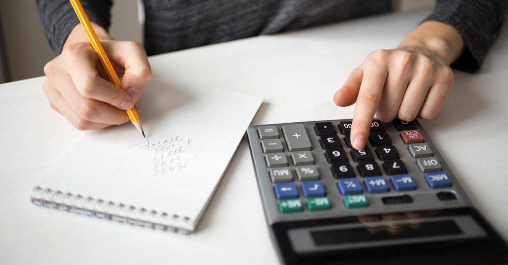 Person using a calculator and writing on paper to calculate monthly loan payments.