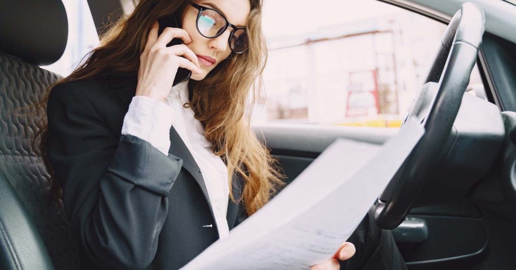 Woman sitting in her car and checking finances on her phone to manage car payments