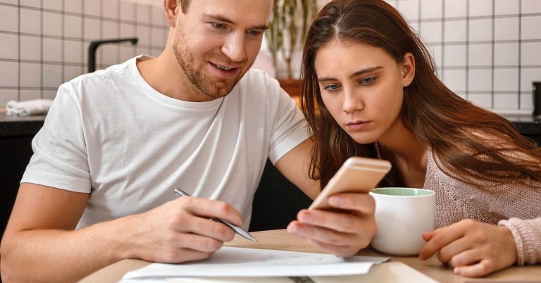 Couple sitting at their kitchen table reviewing mortgage documents and comparing interest rate and APR on a phone