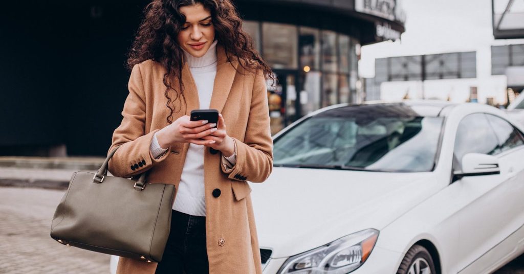 Woman using her phone near a car while checking auto loan preapproval options