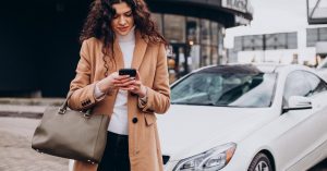 Woman using her phone near a car while checking auto loan preapproval options