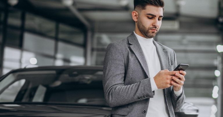Man comparing car loan financing options by phone in a showroom