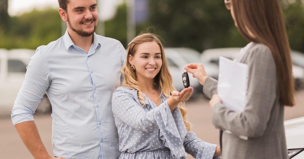 Couple receiving car keys at a dealership while trading in a car with an existing loan