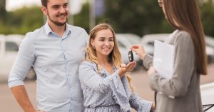 Couple receiving car keys at a dealership while trading in a car with an existing loan