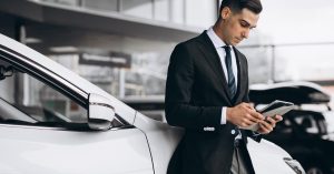 Man checking his phone in a car showroom while reviewing auto loan balance and vehicle value