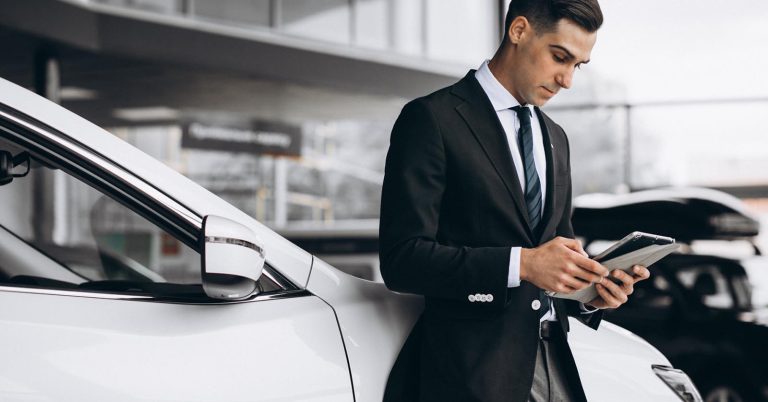 Man checking his phone in a car showroom while reviewing auto loan balance and vehicle value