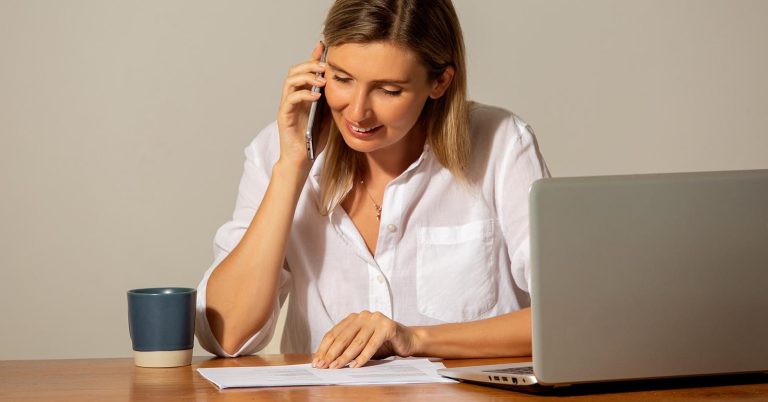 Woman taking a debt collector call while reviewing paperwork at a laptop