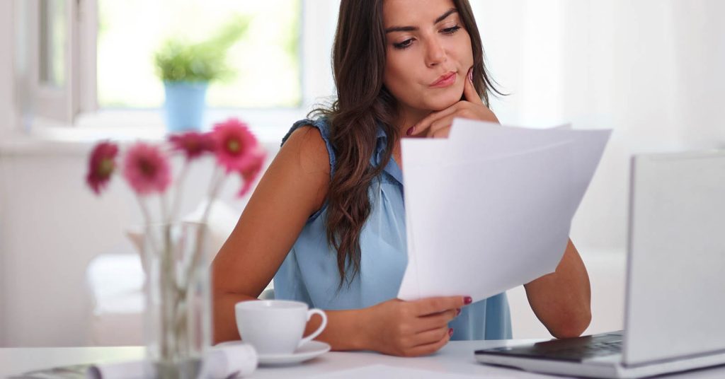 Woman reviewing debt consolidation and debt management plan paperwork at a laptop