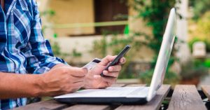 Person holding a credit card and phone while reviewing credit card payments on a laptop