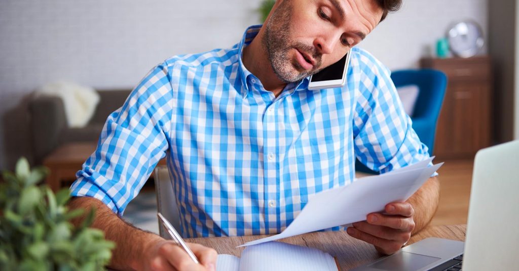 Man calling a creditor while reviewing charged-off debt paperwork