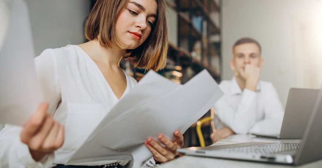 Woman reviewing debt collection documents with a concerned partner nearby