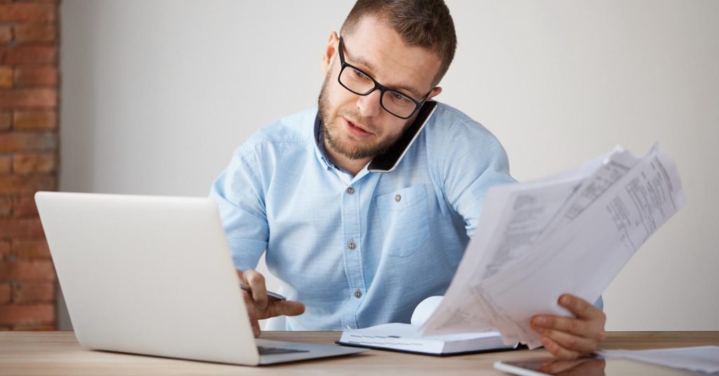 Man reviewing bills while speaking with a credit card company on the phone