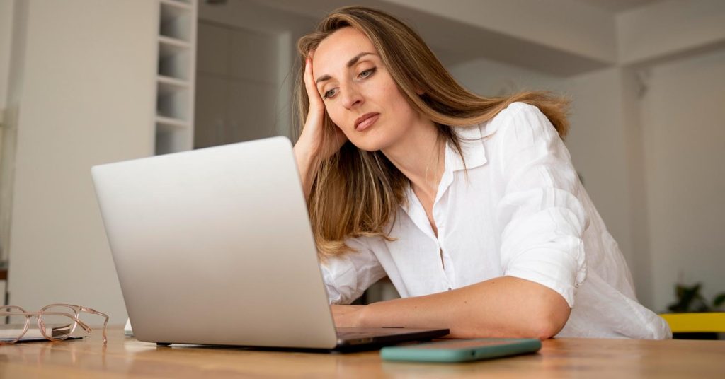 Woman feeling overwhelmed while checking repeated debt collection calls on her phone and laptop