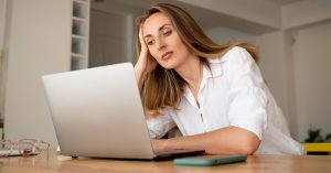 Woman feeling overwhelmed while checking repeated debt collection calls on her phone and laptop