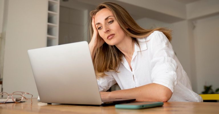 Woman feeling overwhelmed while checking repeated debt collection calls on her phone and laptop