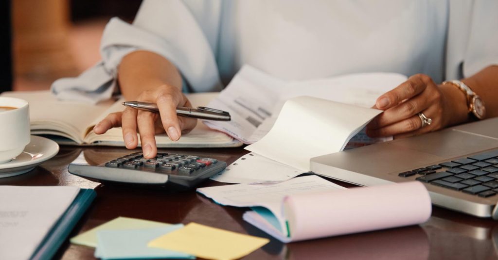 Woman reviewing bills with a calculator and laptop