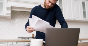 Man reviewing bills while speaking on the phone beside a laptop