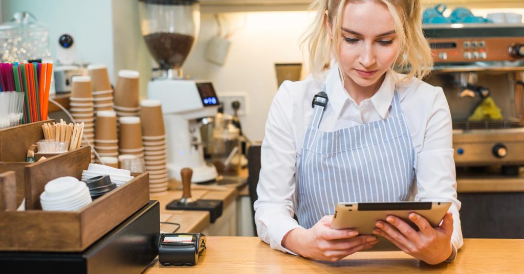 Cafe owner using a tablet at the counter beside a card payment terminal