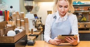Cafe owner using a tablet at the counter beside a card payment terminal