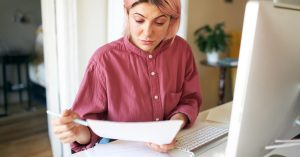 Woman reviewing financial paperwork at a home computer