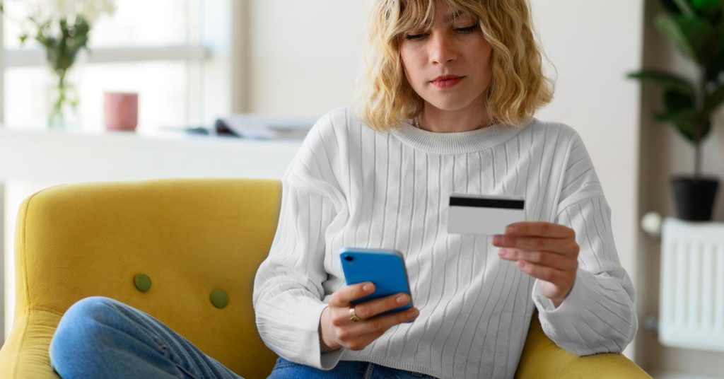 Woman holding a credit card and checking her phone while building credit