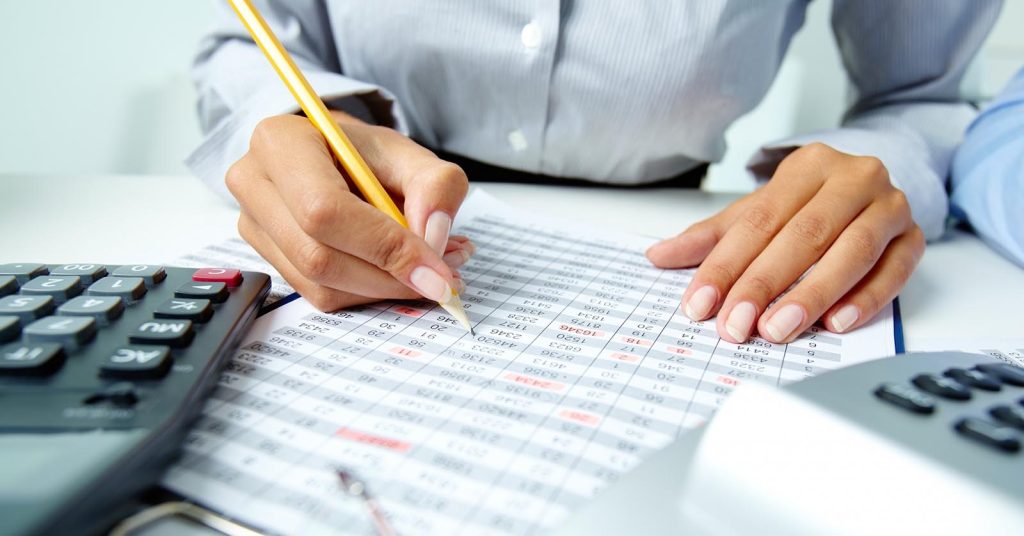 Hands writing on a financial worksheet beside two calculators