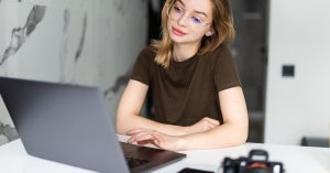 Woman using a laptop at a table with a camera and smartphone nearby