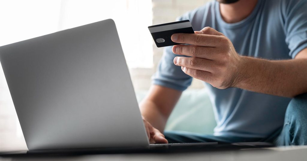 Man reviewing a credit card while using a laptop