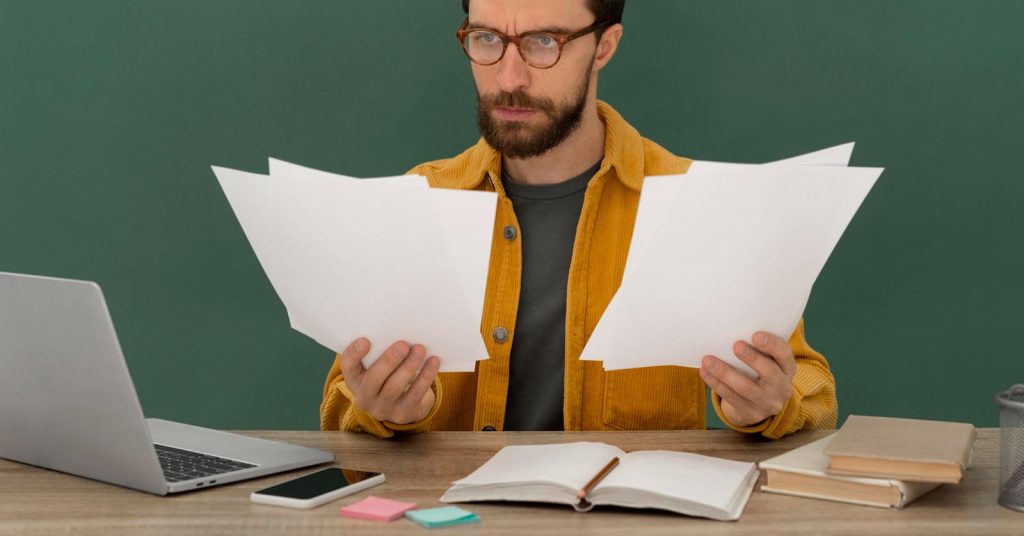 Man reviewing paperwork at a desk beside a laptop