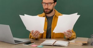Man reviewing paperwork at a desk beside a laptop