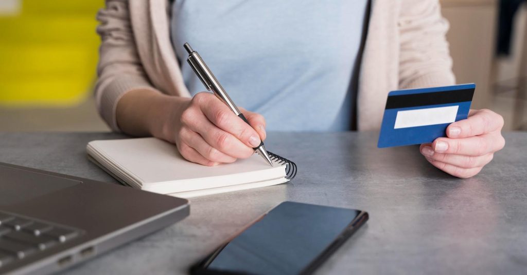 Woman holding a credit card while writing in a notepad at home