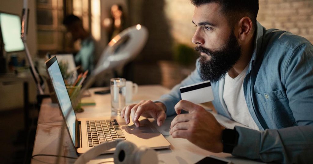 Man holding a credit card while using a laptop