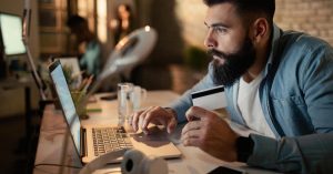 Man holding a credit card while using a laptop