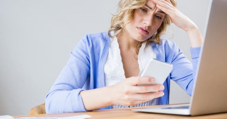 Concerned woman checking a smartphone beside a laptop