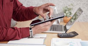 Person reviewing financial documents on a tablet beside a laptop and calculator