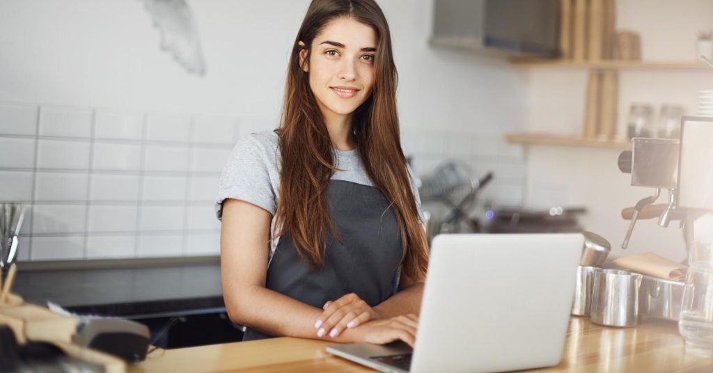 Woman standing behind a counter beside an open laptop