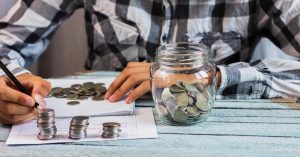 Person counting coins and building a small emergency fund in a glass jar