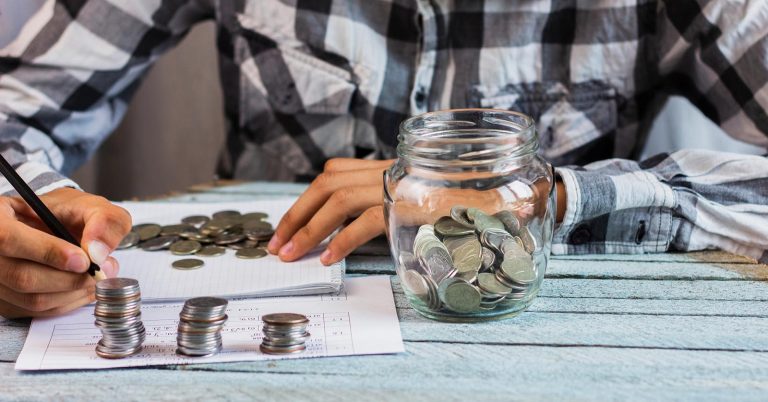 Person counting coins and building a small emergency fund in a glass jar