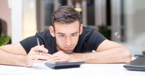 Man leaning over a calculator while reviewing financial paperwork