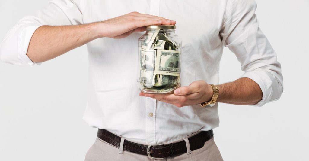 Man holding a glass jar filled with dollar bills