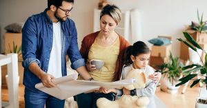 Two adults and a child reviewing a house plan in a room with moving boxes