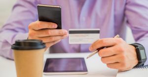 Man holding a payment card and smartphone at a desk
