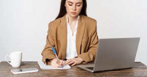 Woman taking notes while reviewing financial information on a laptop