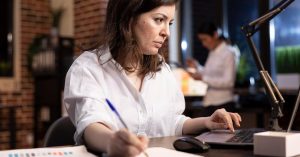 Woman tracking financial progress in a notebook beside a laptop