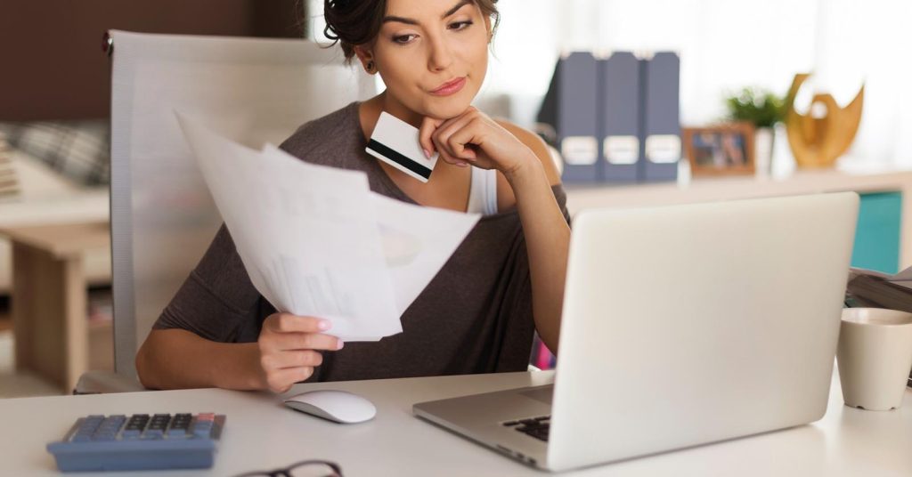 Woman reviewing credit card documents beside a laptop and calculator