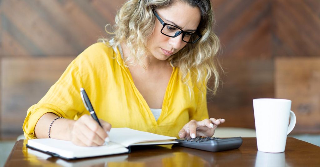 Woman calculating the total cost of a debt settlement plan with a calculator and notebook